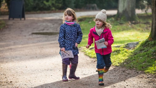 Two small girls in winter wear on a garden path holding trail sheets